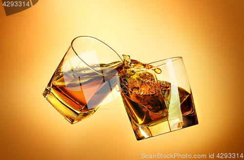 Image of Two whiskey glasses clinking together on brown