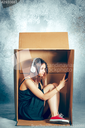 Image of Introvert concept. Woman sitting inside box and working with phone