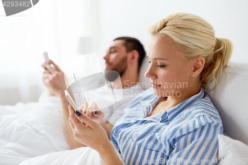 Image of couple with smartphones in bed at home