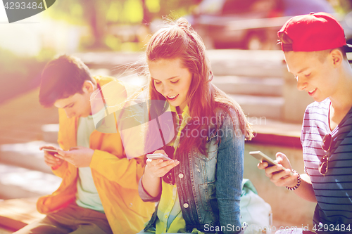 Image of happy teenage friends with smartphones outdoors