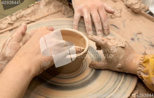 Image of Beginner and teacher hands in clay at process of making crockery