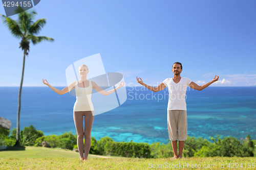 Image of happy couple making yoga exercises on beach