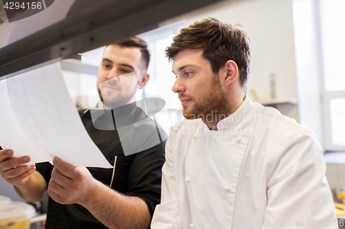 Image of chef and cook with lists or bills at kitchen