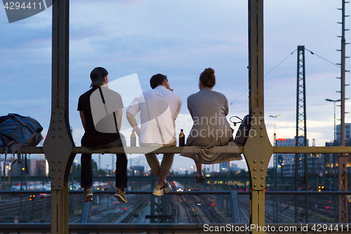 Image of Young friends sitting on urban railway bridge, Munich, Germany.