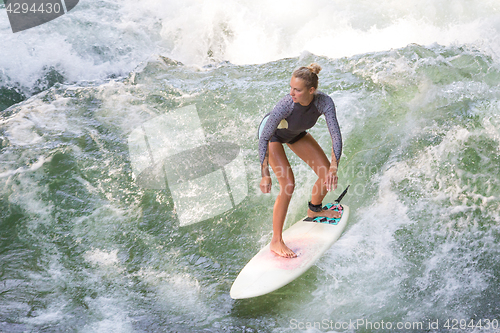 Image of Atractive sporty girl surfing on famous artificial river wave in Englischer garten, Munich, Germany.