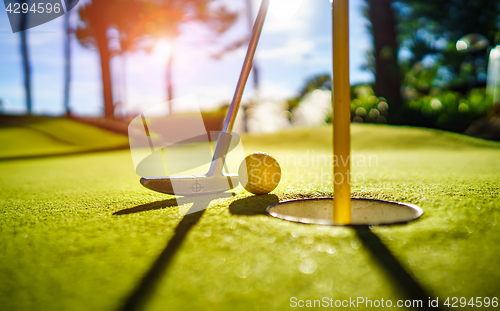 Image of Mini Golf yellow ball with a bat near the hole at sunset