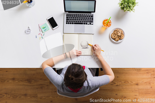 Image of woman with laptop drawing in notebook at office