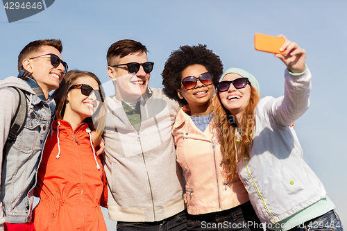 Image of happy friends taking selfie by smartphone outdoors