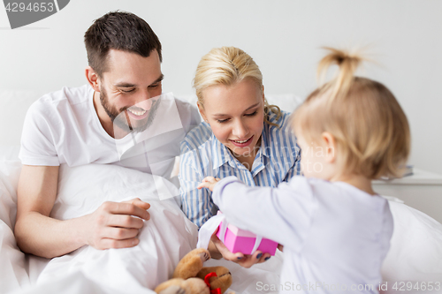 Image of happy family with gift box in bed at home