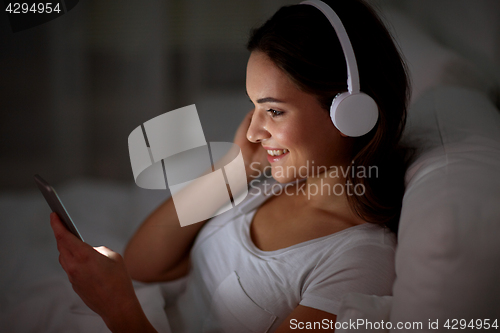 Image of woman with smartphone and headphones in bed