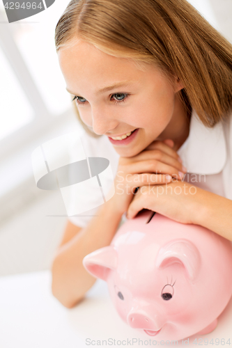 Image of happy girl with piggy bank at home