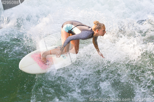 Image of Atractive sporty girl surfing on famous artificial river wave in Englischer garten, Munich, Germany.