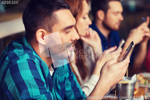 Image of friends with smartphones dining at restaurant