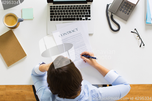Image of businesswoman signing contract document at office