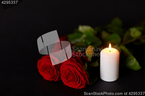 Image of red roses and burning candle over black background