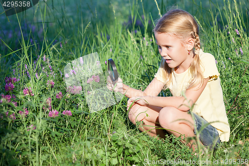 Image of Happy little girl exploring nature with magnifying glass 