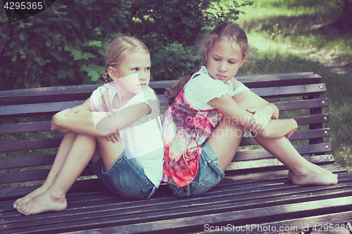 Image of two sad sister sitting on the bench in park 