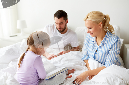 Image of happy family reading book in bed at home