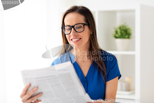 Image of happy woman in glasses reading newspaper at office