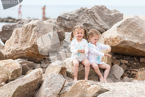 Image of Children on the sea beach. Twins sitting against stones and sea water.