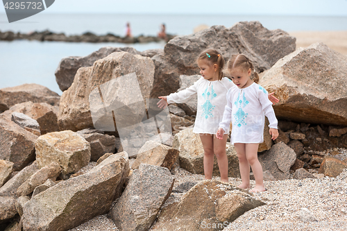 Image of Children on the sea beach. Twins standing against stones and sea water.