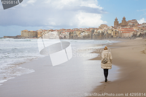 Image of Solitary woman walking the beach of Cefalu in winter time, Sicily, south Italy.