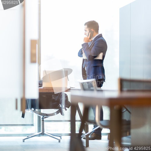 Image of Businessman talking on a mobile phone while looking through window.