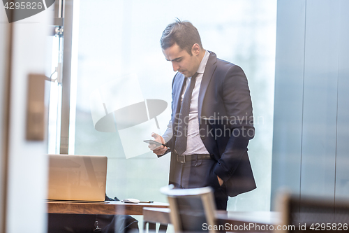 Image of Businessman looking at smart phone in modern corporate office.