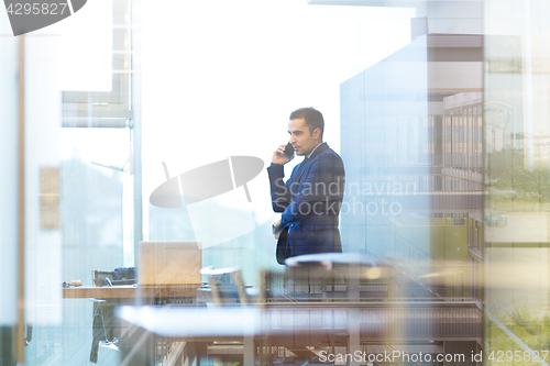 Image of Businessman talking on a mobile phone while looking through office window.