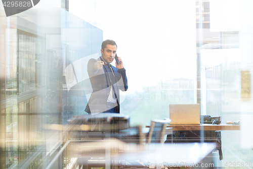 Image of Businessman talking on a mobile phone in corporate office, pointing to camera.