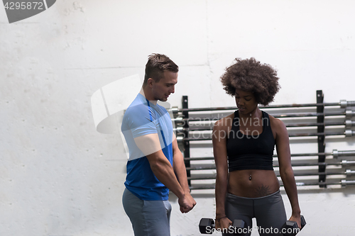 Image of black woman doing bicep curls with fitness trainer