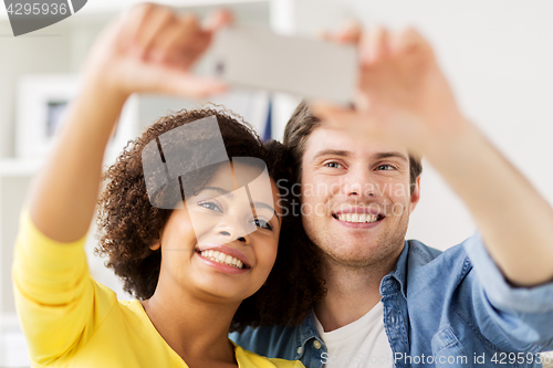 Image of happy couple with smartphone taking selfie at home