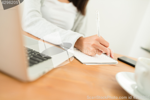 Image of Woman writing on the note book on her desk