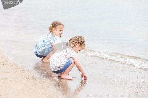 Image of Children on the sea beach. Twins sitting along sea water.