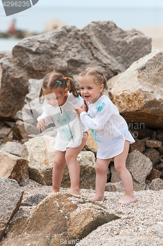 Image of Children on the sea beach. Twins standing against stones and sea water.