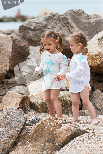 Image of Children on the sea beach. Twins standing against stones and sea water.