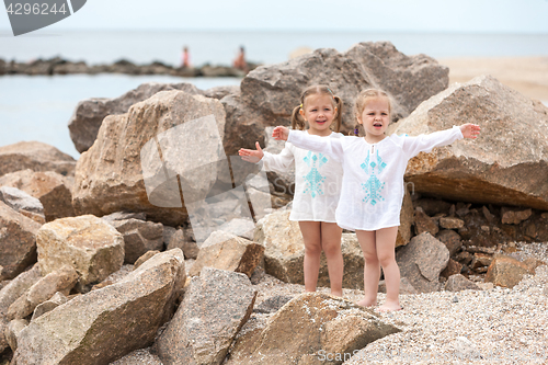 Image of Children on the sea beach. Twins standing against stones and sea water.