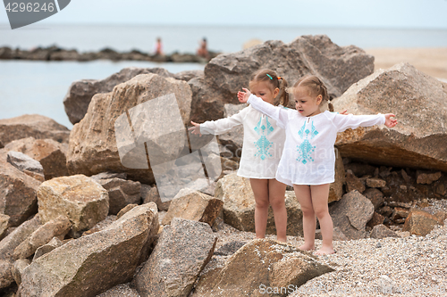 Image of Children on the sea beach. Twins standing against stones and sea water.