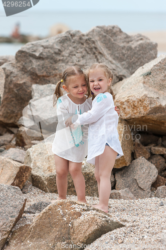 Image of Children on the sea beach. Twins standing against stones and sea water.