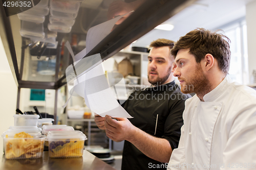 Image of chef and cook with lists or bills at kitchen