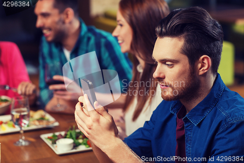 Image of man with smartphone and friends at restaurant