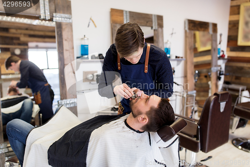 Image of man and barber with trimmer cutting beard at salon