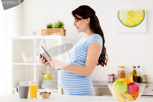 Image of pregnant woman with tablet pc eating at home