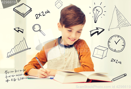 Image of smiling student boy writing to notebook at home