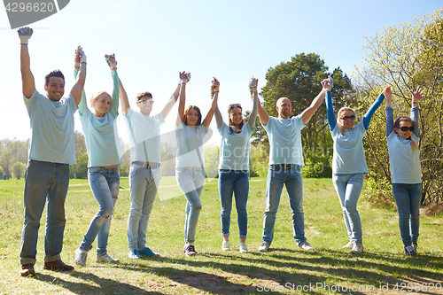 Image of group of happy volunteers holding hands outdoors