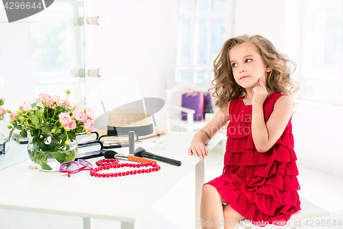 Image of A little girl with cosmetics. She is in mother\'s bedroom, sitting near the mirror.