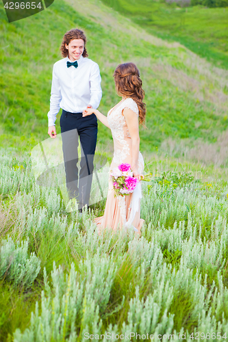 Image of Just married loving couple in wedding dress on green field in a forest at summer