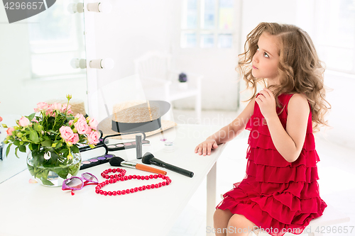 Image of A little girl with cosmetics. She is in mother\'s bedroom, sitting near the mirror.
