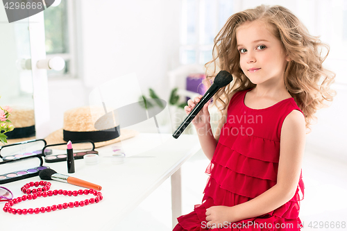 Image of A little girl with cosmetics. She is in mother\'s bedroom, sitting near the mirror.