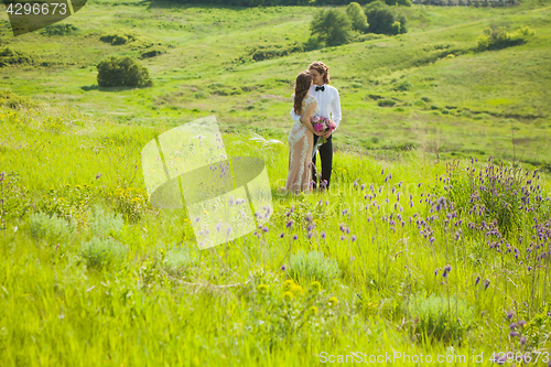 Image of Just married loving couple in wedding dress on green field in a forest at summer